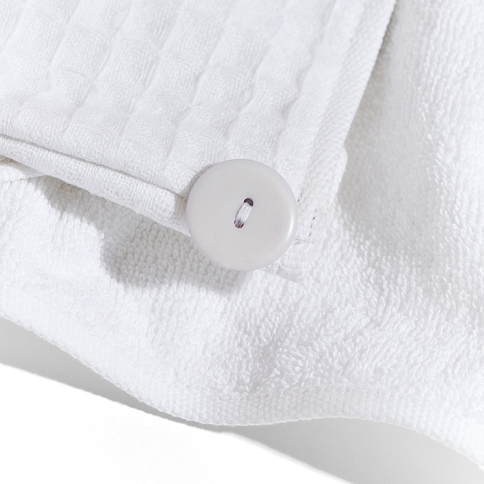 A close-up of Grove Co.s Organic Cotton Hair Towel shows white, textured waffle-patterned fabric with a large white button in the corner. The organic cotton towel rests against a plain white terry cloth background, with the buttons shine contrasting with the matte finish—ideal for taming frizz.
