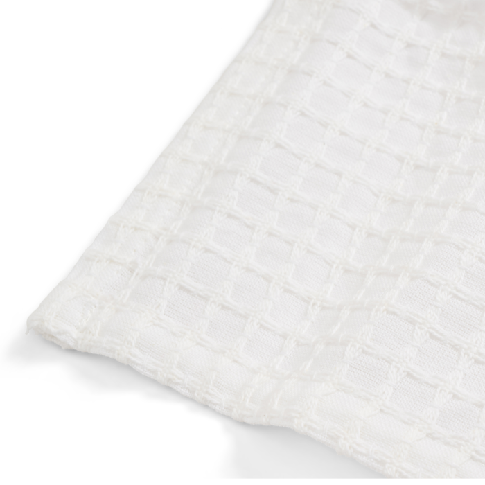 Close-up of Grove Co.s Organic Cotton Textured Kitchen Towels showcasing a white waffle weave reminiscent of absorbent, quick-drying surfaces. The angled view highlights the square texture and subtle shadows on the organic cotton fabric.