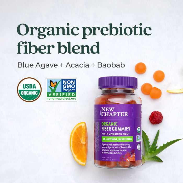 A bottle of New Chapter Organic Fiber Gummies with USDA Organic and Non-GMO Project Verified labels. Surrounded by fruit slices and gummies on a light background. Text reads "Organic prebiotic fiber blend: Blue Agave + Acacia + Baobab.