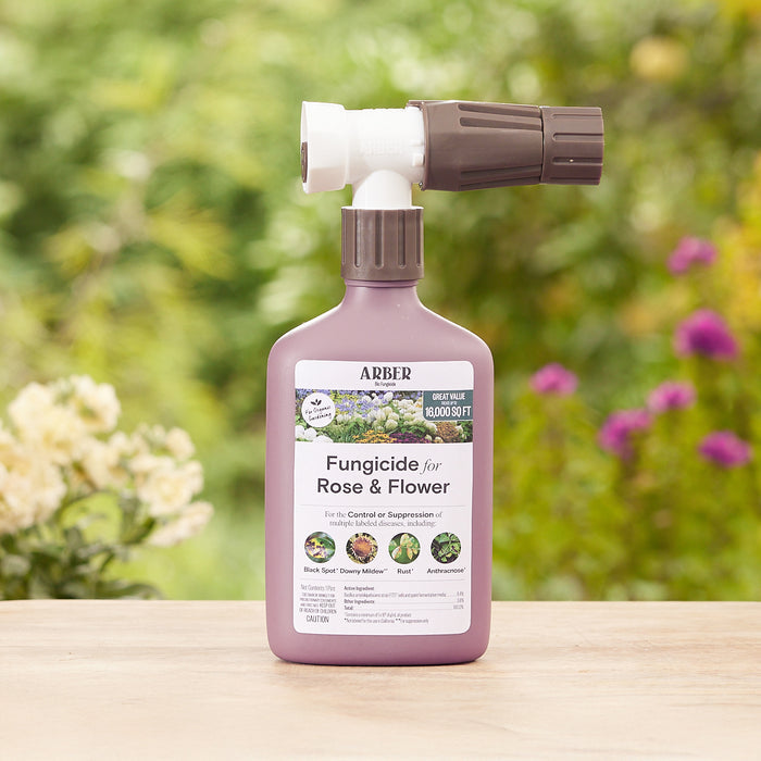 A bottle of Arber Organic Fungicide for Roses and Flowers, RTS sits on a wooden surface against a blurred green garden. It has a spray nozzle and labels showing its use for treating black spot, powdery mildew, downy mildew, and rust.