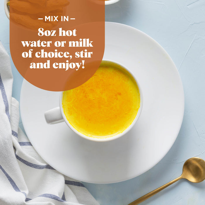 A cup of golden yellow liquid, likely a turmeric latte, sits on a white saucer. A gold spoon rests nearby on a light blue surface. Text above the cup reads, "Mix in 8oz hot water or milk of choice, stir and enjoy!" A striped cloth is nearby.