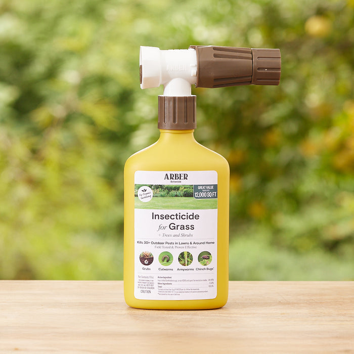 A yellow bottle of Arbers Organic Insecticide for Lawn, Tree, and Shrub, RTS with a brown spray nozzle sits on wood. Its labeled to kill 30+ lawn pests without chemicals. Blurred greenery is in the background.