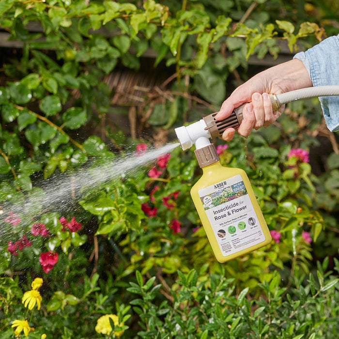 A person uses Arbers Organic Insecticide for Rose and Flowers RTS to spray plants in a garden, surrounded by vibrant blooms and lush greenery, ensuring theyre protected against outdoor pests while maintaining a flourishing haven.