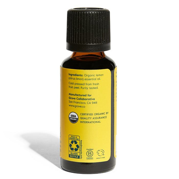 A dark amber glass bottle with a black cap features a yellow label reading Organic Lemon Essential Oil - Uplifting Aromatherapy. Details about ingredients and manufacturing by Grove Co. in San Francisco are present, along with certification logos and a website link.