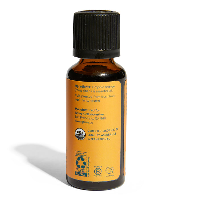 A small brown glass bottle with a black cap features an orange label identifying it as Grove Co.s Organic Orange Essential Oil - Energizing Aromatherapy, noted for being certified organic. Company details and certifications are visible, and the bottle casts a soft shadow on a white background.