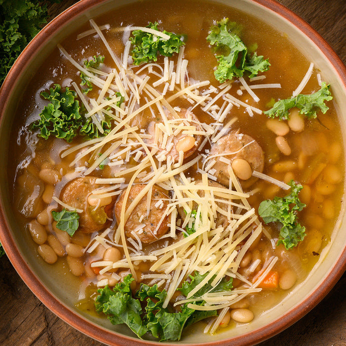 bowl of soup with beans, sausage, and greens on a wooden table