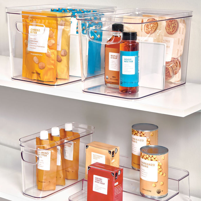 Organized pantry shelves with iDesigns Organizer Bins with Handles (made from recycled plastic) hold assorted packaged foods like cheese bites, almond butter, and more. The compact modular design ensures containers are neatly arranged for easy access.