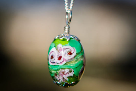 Oval glass flower pendant in green with white and pink blooms, infused with cremains on a silver chain.