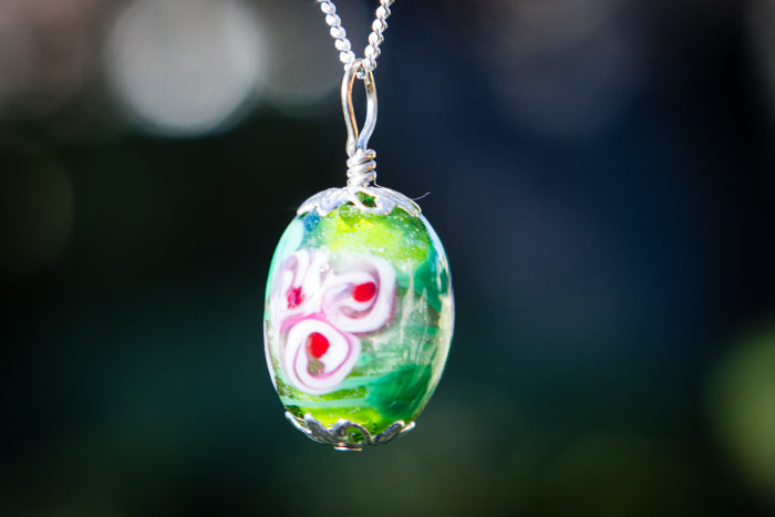 Oval glass flower pendant on a silver chain with a green base and pink white flower, infused with cremation ash.