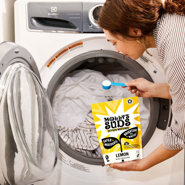 Someone adds Molly’s Suds Oxygen Whitener into a washing machine with white laundry, holding the yellow package beside the open washer.