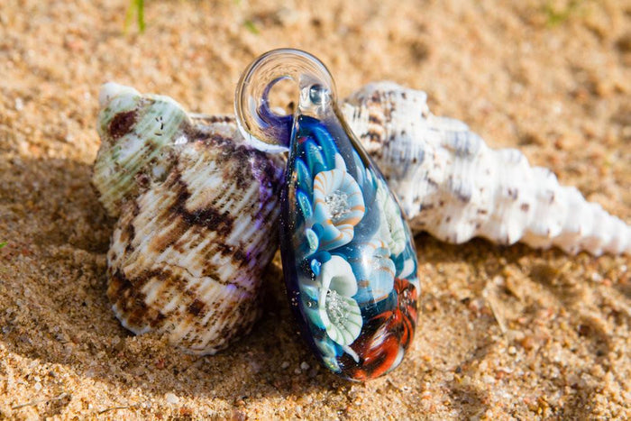 Glass coral reef pendant on sandy beach with blue hues and colorful polyp clusters infused with cremation ashes