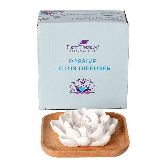 A white ceramic lotus-shaped diffuser sits elegantly on a beech wood tray next to a blue box labeled Plant Therapy: Passive Lotus Diffuser, adorned with a serene purple and blue lotus design.