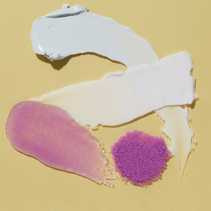 Swashes of VOESH New Yorks Pedi Moments on a yellow background evoke a spa experience, with a light blue smear, white cream, shimmering pink gloss, and a small pile of purple powder.