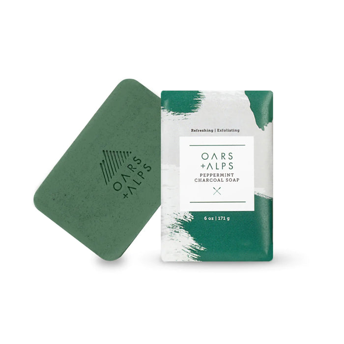 A 6 oz. green Oars + Alps Charcoal Bar Soap, shown beside its white and green Peppermint Charcoal Soap packaging. Infused with peppermint oil and activated charcoal for a refreshing, invigorating cleanse.
