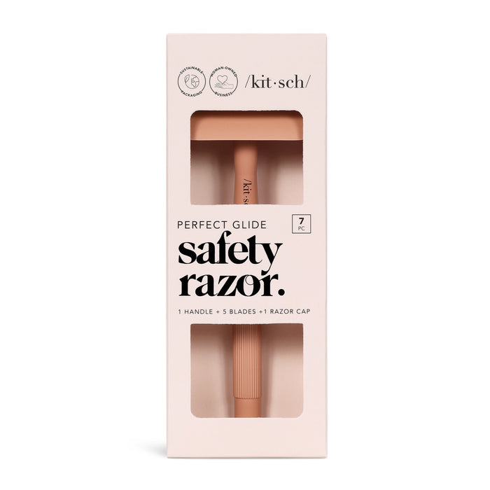 The beige packaging of Kitschs Perfect Glide Safety Razor is plastic-free and includes 1 handle, 5 stainless steel blades, and a razor cap. It mentions seven pieces total, with the muted pink razor visible through a window.