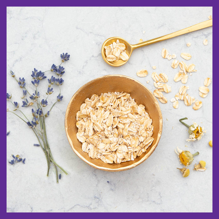 The New Chapter Perfect Postnatal™ Multivitamin rests on a marble surface with lavender and chamomile, a golden spoon hinting at nourishment. Elegantly bordered in purple, the image evokes the gentle care akin to energy, mood, and lactation support.