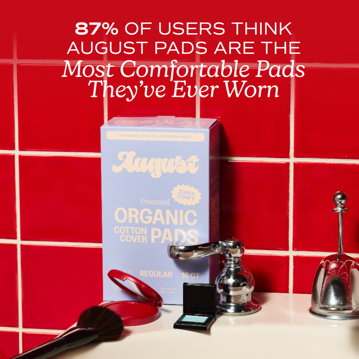 A box of August Night Pads rests on a red-tiled counter with a mirror, hairbrush, compact, and perfume. Above, text reads: 87% of users say August Night Pads are the most comfortable pads they've ever worn.