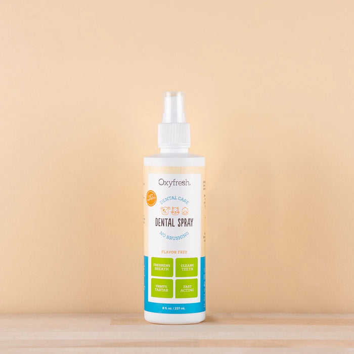 An Oxyfresh Pet Bad Breath Fast Acting Dental Spray rests on a beige backdrop, promoting veterinarian-approved, flavor-free plaque removal. The label emphasizes its breath-freshening and teeth-cleaning power, making it a must-have for pet dental care.