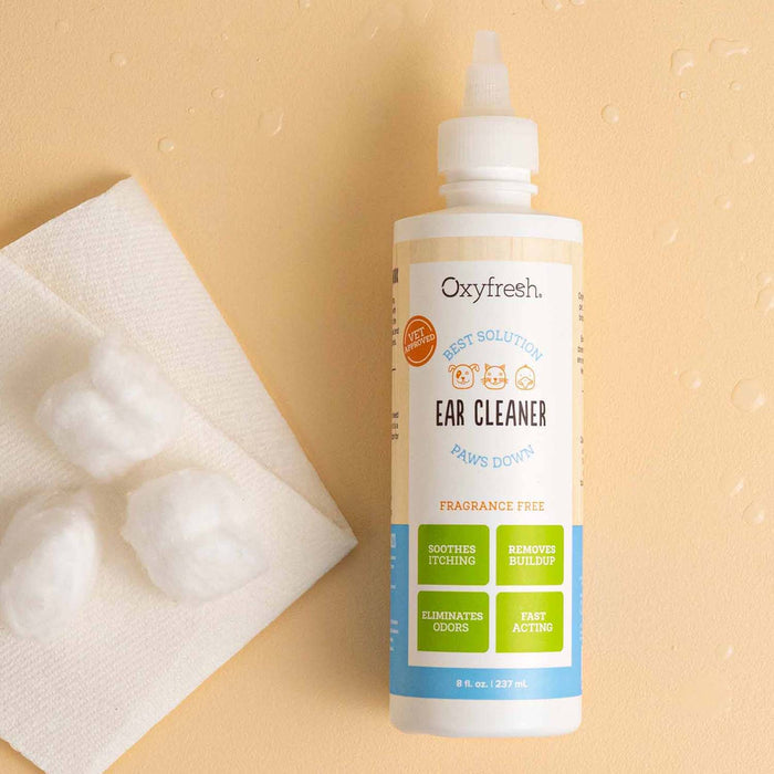 An Oxyfresh Pet Ear Cleaner Yeast-Fighting Ear Wash bottle is on a light surface with a paper towel and three cotton balls nearby. This solution soothes itching, removes buildup, eliminates odors, and works quickly, making it ideal for cleaning dog ears.
