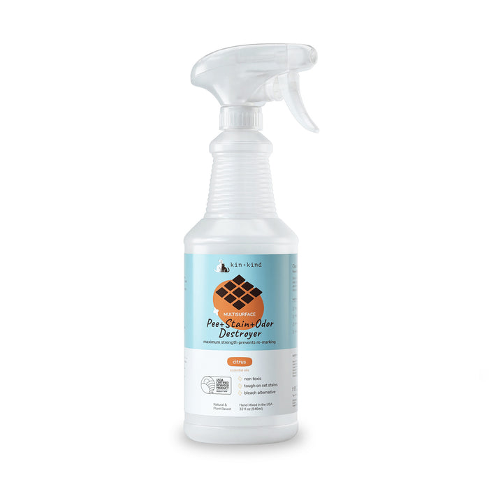 Clear plastic spray bottle with a trigger nozzle labeled kin+kind Pet Pee + Stain + Odor Remover Multi-Surface Spray, featuring a dog footprint graphic. Highlights natural ingredients and plant-based technology using naturally derived zinc salt for effective pet stain and odor removal, citrus scent.