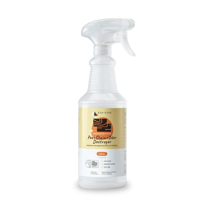 The kin+kind Pet Pee + Stain + Odor Remover Spray for Hardwood Floors comes in a white spray bottle with an orange and black label featuring a dogs head. It has a trigger nozzle and uses plant-based technology with naturally derived ingredients for superior odor elimination with a citrus scent.