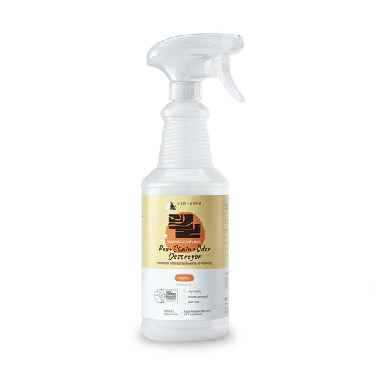 The kin+kind Pet Pee + Stain + Odor Remover Spray for Hardwood Floors comes in a white spray bottle with an orange and black label featuring a dogs head. It has a trigger nozzle and uses plant-based technology with naturally derived ingredients for superior odor elimination with a citrus scent.