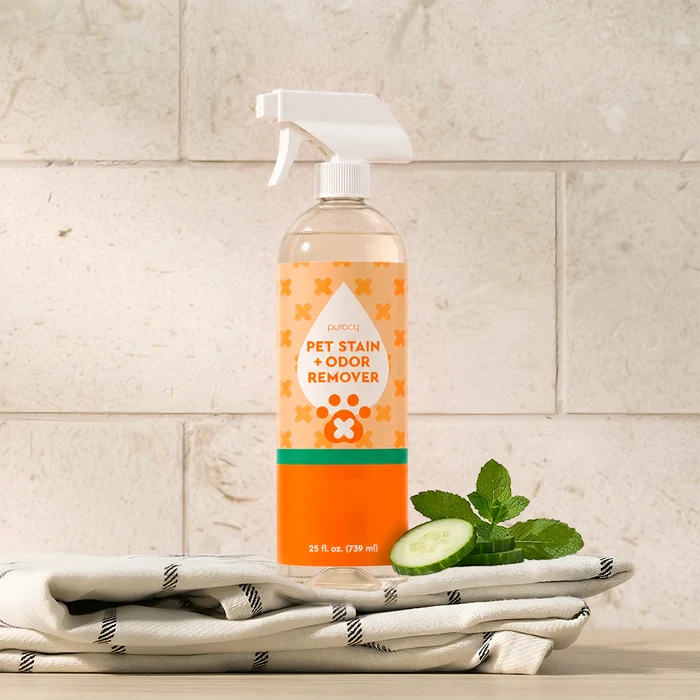 A bottle of Pet Stain & Odor Remover sits on a towel with mint leaves and cucumber slices.
