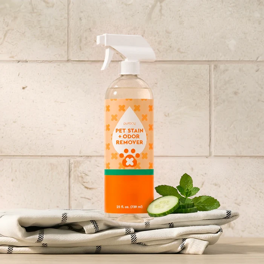 A bottle of Pet Stain & Odor Remover sits on a towel with mint leaves and cucumber slices.
