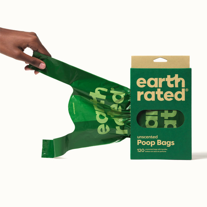 A hand pulls a green bag from an Earth Rated box of Pet Waste Bags with Handles. The eco-friendly green and beige box, crafted from recycled plastic, contains 120 unscented and 100% leak-proof bags with a cut-out displaying the bags inside.