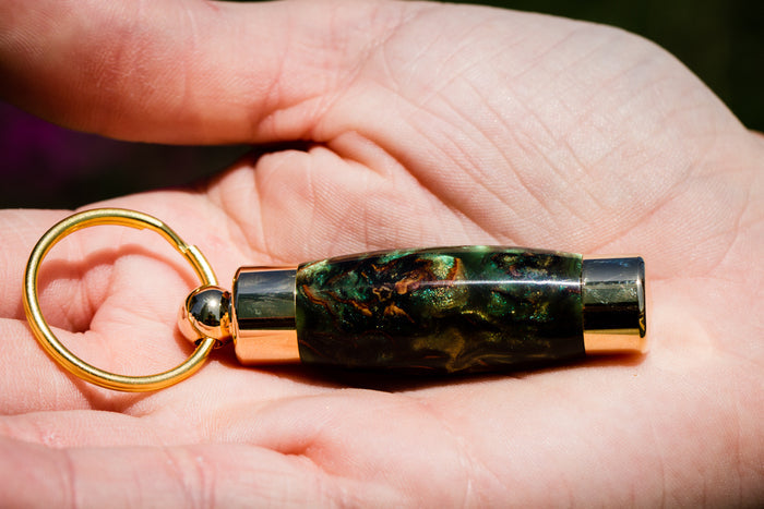 Green marbled acrylic keepsake pendant with gold ends held in a hand.