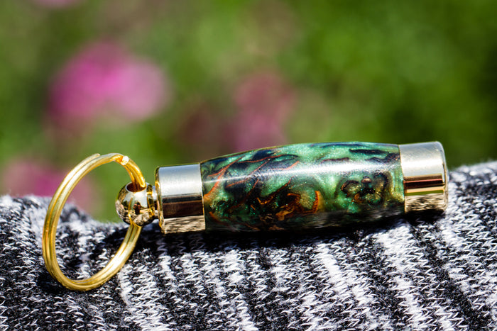 Blue green marbled acrylic keepsake pendant with silver ends and gold ring on denim background.