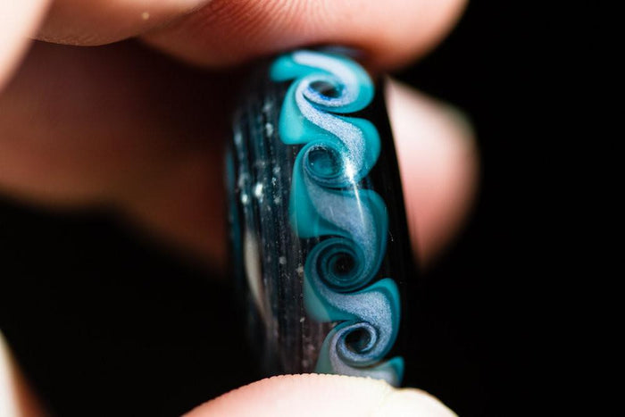 Close-up of aqua Pinwheel Touchstone edge with teal swirling patterns held between fingers.