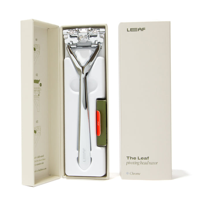 Open box featuring the Plastic Free Razor by Leaf Shave, with a chrome pivoting head for sensitive skin. All-metal build ensures durability, includes slots for replacement blades and instructions inside. Packaging displays Leaf branding.