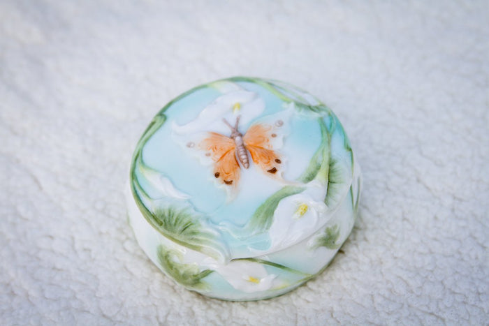 Round porcelain keepsake urn with pale blue glaze featuring an orange butterfly among green leaves
