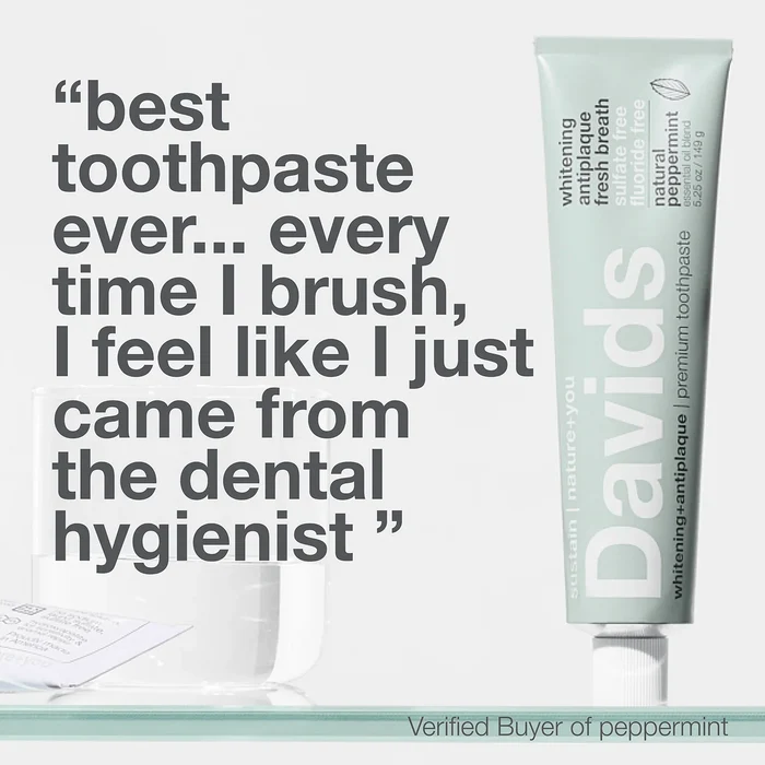 A tube of Davids Premium Toothpaste - Whitening + Antiplaque stands upright next to a clear glass. Large text features a customer review, praising the fluoride free formula and noting it feels like a dental hygienist cleaning. “Verified Buyer of peppermint” appears at the bottom.
