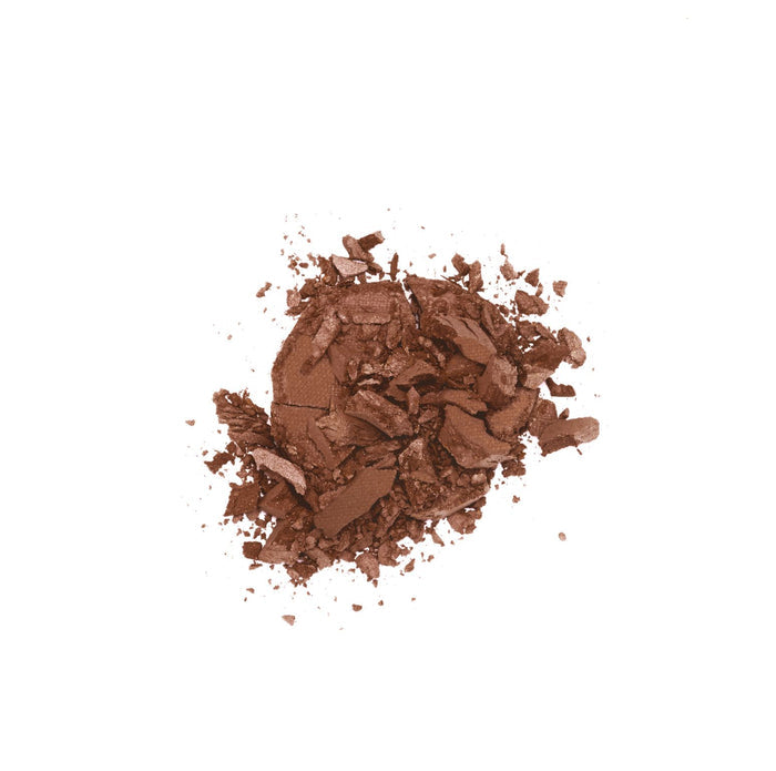 Lily Lolos Pressed Bronzer, with its natural mineral blend, scatters in an uneven mix of fine dust and larger fragments across a white background, evoking a sun-kissed glow.