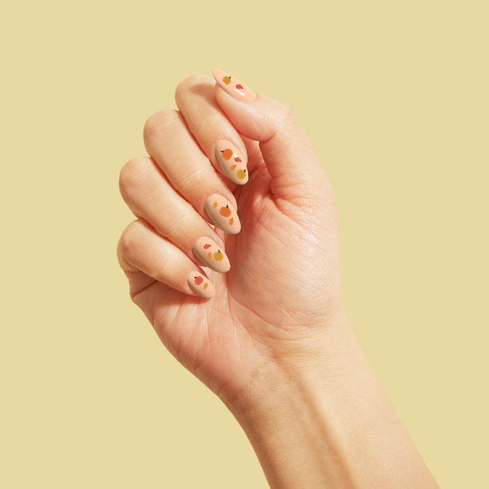 A neatly manicured hand displaying VOESH New Yorks Pumpkin Pie Duo with Nail Stickers, featuring a beige base and abstract red and orange designs, is set against a light beige background, embodying autumns essence.