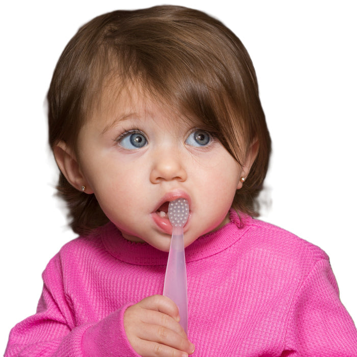 A young child with brown hair and blue eyes, wearing a pink sweater, holds the Radius Pure Brush 6 mo+, an eco-friendly baby toothbrush, in their mouth against a white background.