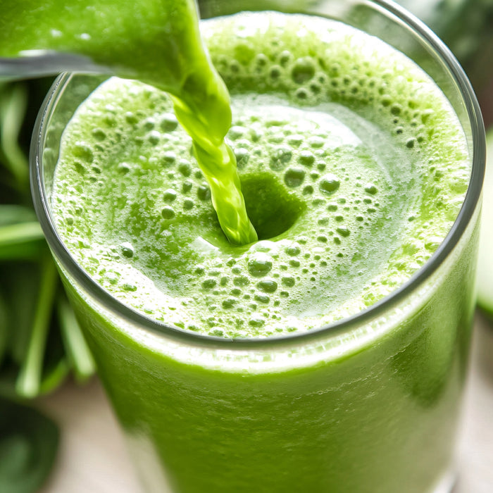 A close-up of green juice made with Kuli Kuli Foods Pure Moringa Organic Superfood Powder being poured into a clear glass, creating frothy bubbles, with fresh green leaves in the background.