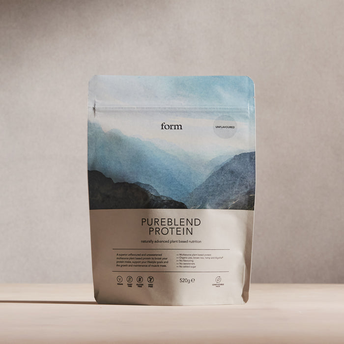 A beige and blue packet of Form Nutritions Pureblend Protein, labeled unflavored, stands with a mountain design on a plain background. It highlights vegan protein powder, organic pea protein, a complete amino acid profile, and eco-friendly packaging.
