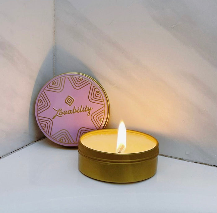 The ThreePlay Massage Candle by Lovability, in a round gold tin with a pink geometric-patterned lid, sits in the rooms corner. Its gentle light enhances the subtle marble-textured walls, creating an ambiance perfect for indulging in a sensual massage oil experience.