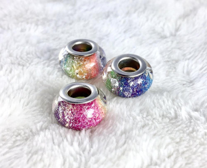 Four rainbow speckled cremation ash beads with metal cores on a white surface.