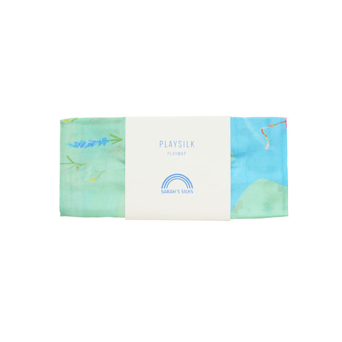 A folded playsilk in blue, green, pink, and yellow hues bears a white label with Sarahs Silks logo and Rainbowland Play Map. This vibrant item fosters imaginative play, sparking creativity in every childs adventure.