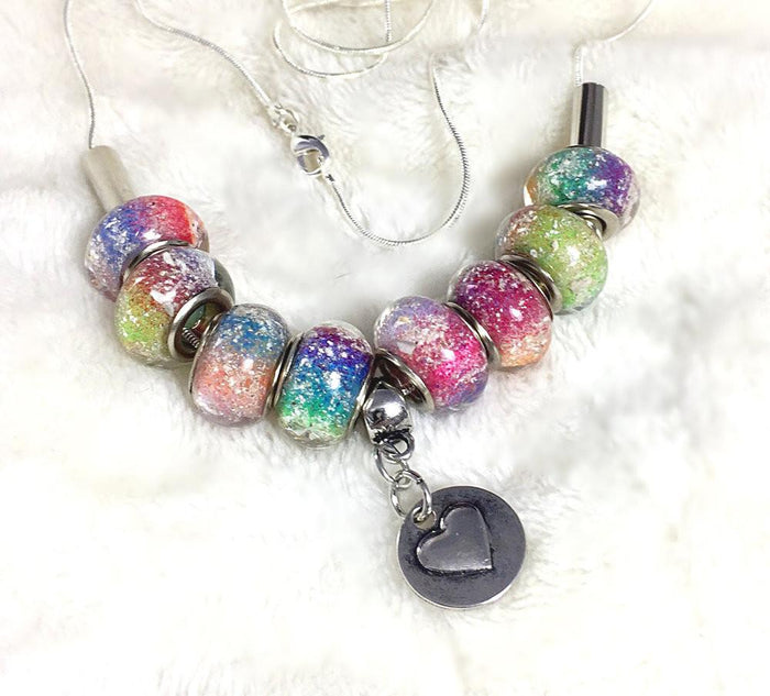 Rainbow's Bridge necklace with eight infused beads and a heart charm displayed on white fur background