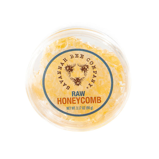 Top-down view of a picnic-sized round container labeled Savannah Bee Company Raw Honeycomb Picnic Round Net Wt. 3.17 oz (90 g), filled with energizing honeycomb pieces and adorned with charming bee illustrations.