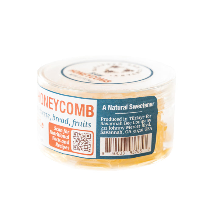 The Raw Honeycomb Picnic Round by Savannah Bee Company is a clear plastic container of energizing honeycomb, labeled as a natural sweetener ideal for pairing with cheese, bread, and fruits. It features an address in Savannah, GA, USA, along with a barcode for nutritional facts and recipes.