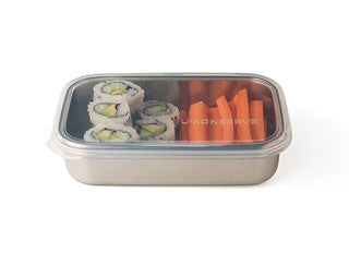 The U-Konserve Rectangle Container, made of stainless steel with a leak-proof lid, holds sliced avocado sushi rolls on one side and carrot sticks on the other, making it perfect for plastic-free food storage.