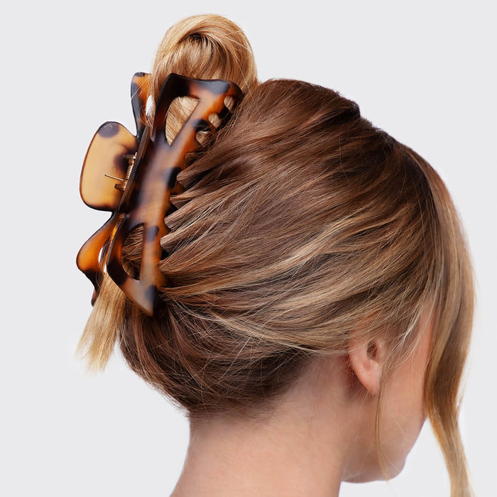 A woman with light brown hair styled in a loose bun is featured against a white background, secured by the Kitsch Recycled Plastic Jumbo Claw Clip with a tortoiseshell pattern, emphasizing its chic design and eco-friendly composition.