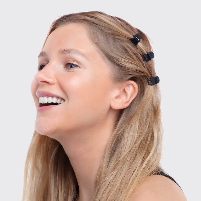 A woman with long blonde hair smiles, looking to the side. In her hair, she wears a Kitsch Recycled Plastic XS Claw Clip Set and a black tank top against a plain white background.