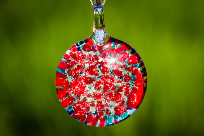 Round glass pendant infused with cremation ashes featuring red and blue marigold petals on a silver chain
